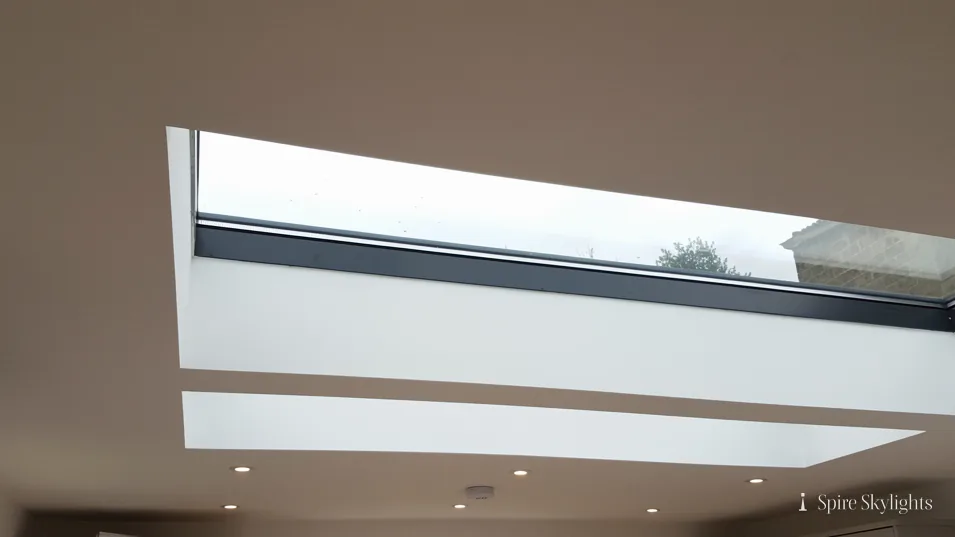 Long, slim flat rooflight set in a plastered ceiling with downlights