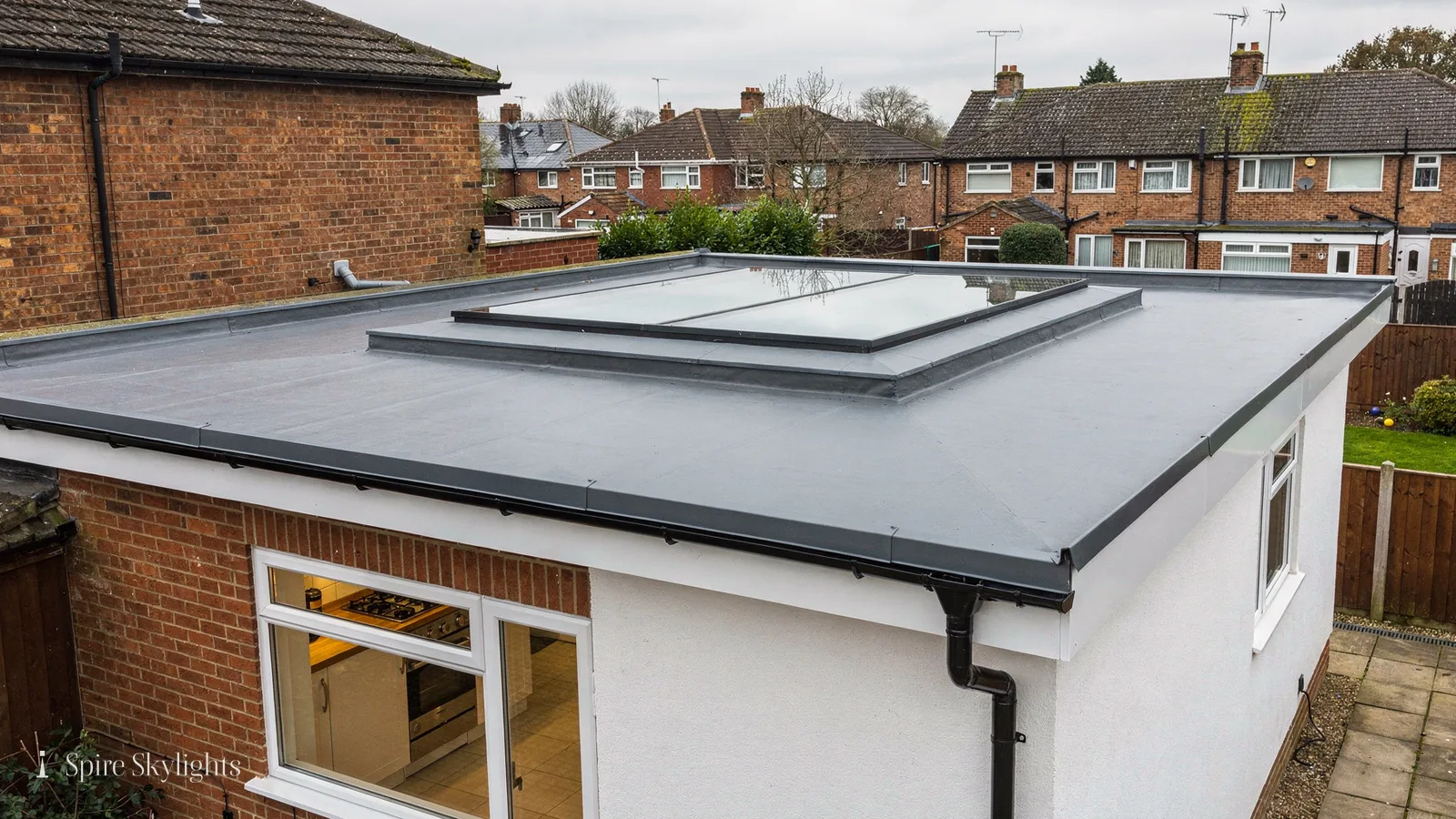 Rendered flat-roof extension with a rooflight, behind a row of red-brick houses