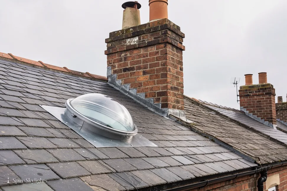 Sun tunnel dome on a slate roof beside a brick chimney