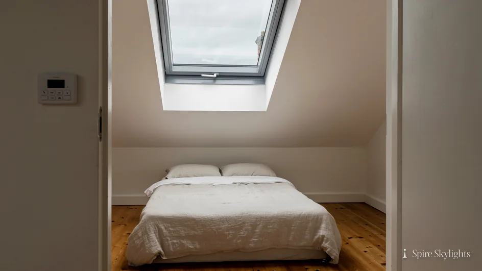 Loft bedroom through the doorway, an electric roof window open in the slope and its wall control by the door